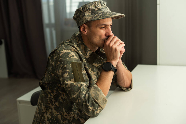 Ein deprimierter Armeeangehöriger in Uniform sitzt in einem leeren Raum. Platz für Ihr Poster an der Wand. Hochwertiges Foto - Foto, Bild