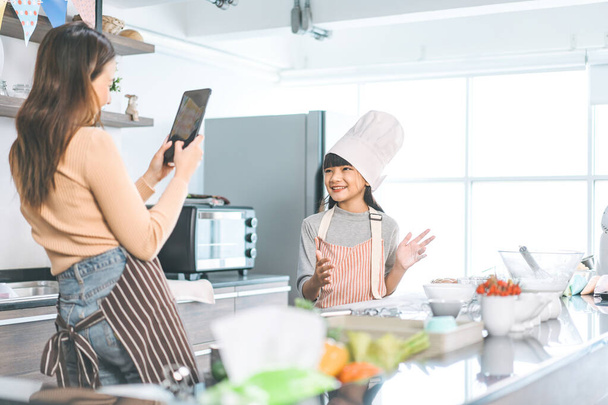 Mutlu Asyalı anne ve kızı mutfakta yemek pişiriyor. Sosyal medya için akıllı telefonlu selfie. Evdeki boş yaşam tarzları. Faiz becerisi olan çocuk büyümesi. - Fotoğraf, Görsel