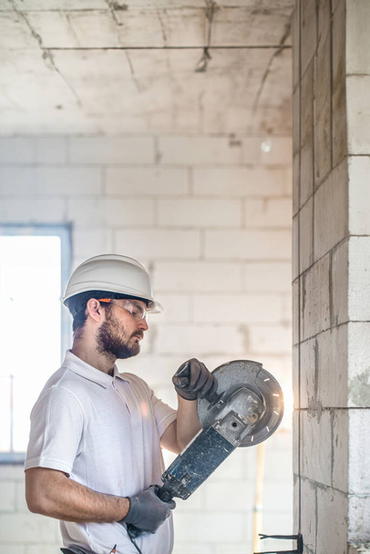 The industrial Builder works with a professional angle grinder to cut bricks and build interior walls. Professional on the construction site. - Photo, Image