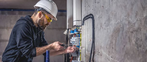 Un electricista masculino trabaja en una centralita con un cable de conexión eléctrica. Copiar espacio. - Foto, imagen