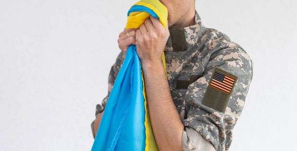 Bandera Americana en el brazo de los soldados y la bandera de Ucrania en el fondo. Apoyo militar de Estados Unidos Ucrania. - Foto, imagen