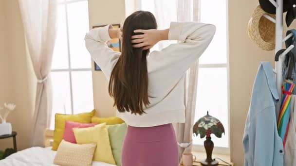 Fiatal spanyol nő nyújtózkodik egy napos hálószoba, körülvéve színes dekoráció és alkalmi otthoni viselet. - Felvétel, videó