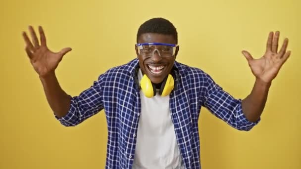 Homem americano africano alegre vestindo óculos de segurança celebrando a vitória com expressão alegre e sorriso feliz, em pé sobre fundo isolado amarelo. emoção e triunfo manifesto! - Filmagem, Vídeo