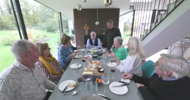 Ces images de stock chaleureuses et invitantes capturent une famille dégustant un repas ensemble autour d'une grande table dans une maison moderne et bien éclairée. L'atmosphère décontractée est remplie de conversation et de convivialité - Séquence, vidéo