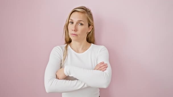 Skeptic young blonde damning with a nervous and disapproving facial expression, standing with arms crossed over isolated pink background - Footage, Video