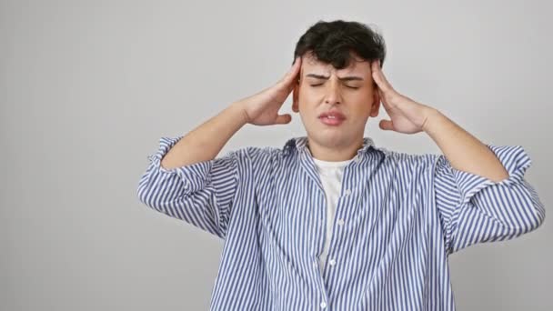 Young man, stressed-out in striped shirt, suffering a migraine headache from the pressure. he's standing, isolated against a white wall, hand on head, face expressing sad desperation. - Footage, Video