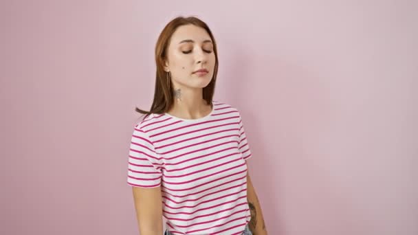 Besorgtes junges brünettes Mädchen in gestreiftem T-Shirt, das die Uhrzeit auf seiner Armbanduhr überprüft, schaut beunruhigt über die Möglichkeit einer späten Ankunft für ein Treffen vor isoliertem rosa Hintergrund. - Filmmaterial, Video