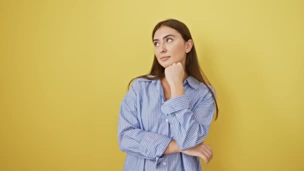 Thoughtful young hispanic woman with a serious face, chin rested on hand, wrestling with a confusing idea, isolated on a yellow background, her beautiful expression betraying an underlying doubt. - Footage, Video