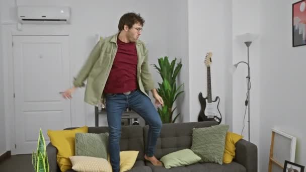 Ein fröhlicher Mann tanzt barfuß in einem gemütlichen Wohnzimmer und spiegelt Glück und Muße zu Hause wider. - Filmmaterial, Video