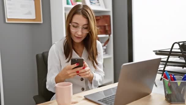 Femme caucasienne dans des lunettes, se sentant réussie à son lieu de travail de bureau moderne avec ordinateur portable et smartphone. - Séquence, vidéo