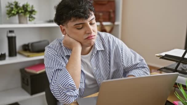 Düşünceli genç bir adam, modern bir çalışma ortamının ortasında bir ofiste dizüstü bilgisayarla oturup sıkıntısını ya da yorgunluğunu gösterir.. - Video, Çekim