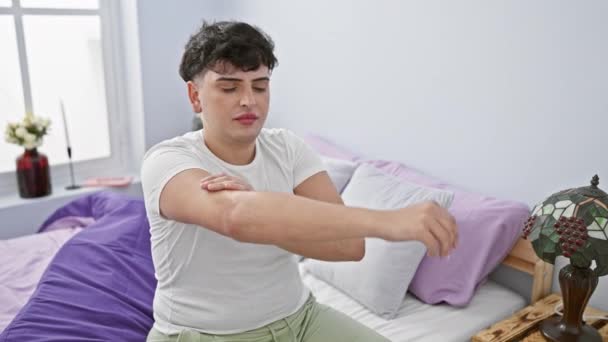 Un giovane applica lozione alle braccia mentre è seduto su un letto in una camera da letto con arredamento moderno. - Filmati, video