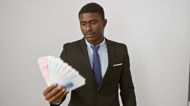 Hombre afroamericano confiado y alegre en un traje, sonriente sonrisa dentada, sosteniendo billetes de yuan chinos. mirando positivo y acertado sobre fondo blanco aislado. - Metraje, vídeo