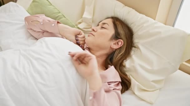 Egy fiatal nő nyújtózkodik az ágyban, egy fényesen megvilágított hálószobában ébred, a reggeli frissesség érzetét keltve.. - Felvétel, videó