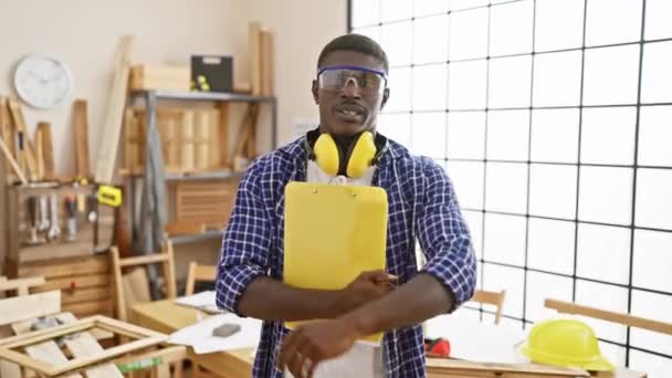 Уверенный человек в защитных очках и наушниках держит планшет в яркой столярной мастерской - Кадры, видео