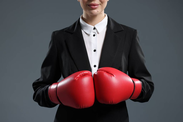 Businesswoman in suit wearing boxing gloves on grey background, closeup - Φωτογραφία, εικόνα