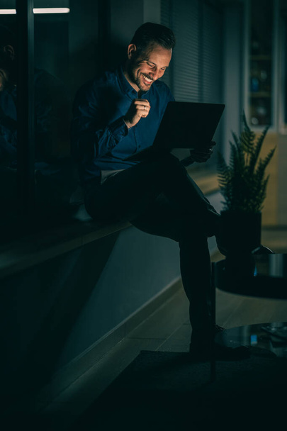 Nuori liikemies istuu laukkutuolissa ja käyttää digitaalista tablettia onnistuneen työpäivän jälkeen.Juhli menestystä. - Valokuva, kuva