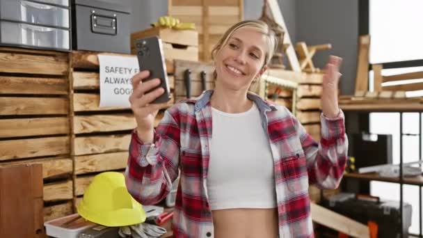 Hymyilevä nainen ottaa selfien työpajassa, jossa on puuntyöstötyökaluja, turvavarusteita ja puulankkuja.. - Materiaali, video