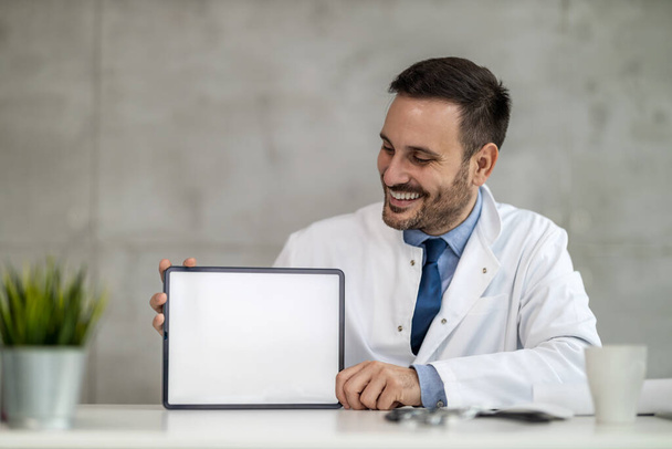 Porträt eines jungen männlichen Arztes, der ein digitales Tablet in der Hand hält und den freien Raum zeigt.. - Foto, Bild