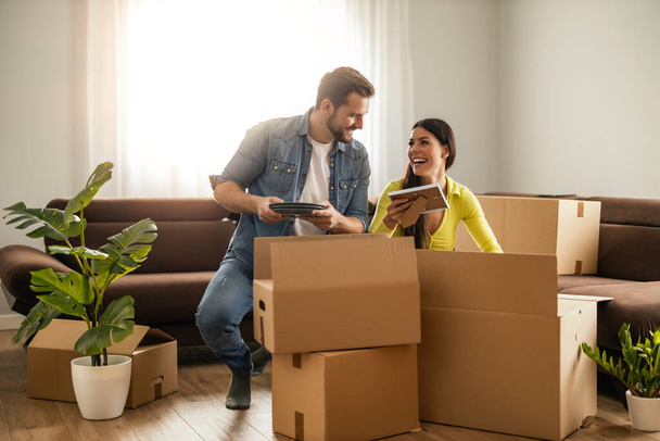 Glückliches junges Ehepaar zieht in neue Wohnung und packt gemeinsam Kisten aus. - Foto, Bild