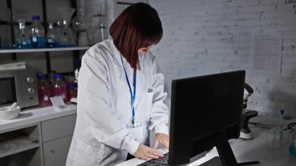 Kypsä laboratoriotakkinen naistutkija käyttää tietokonetta tutkimuslaboratoriossa, viestittää ammattimaisuudesta ja asiantuntemuksesta. - Materiaali, video