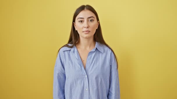 Schöne junge hispanische Frau steht staunend mit weit aufgerissenem Mund in schockierter Ungläubigkeit und trägt Hemd auf isoliertem gelben Wandhintergrund - Filmmaterial, Video