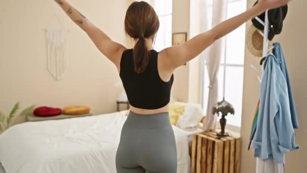 Een jonge vrouw strekt zich uit in een gezellige slaapkamer interieur, belichaamt wellness en ochtend routines. - Video