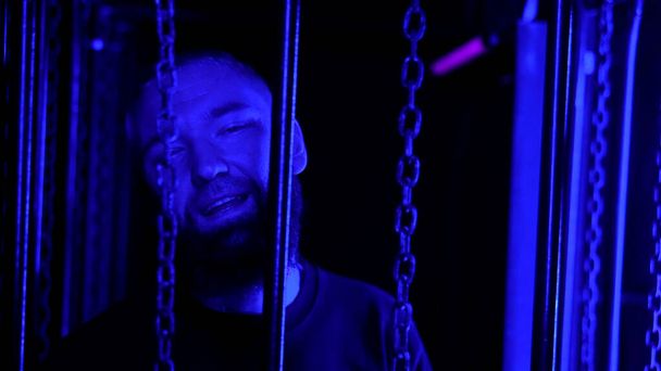 Stilvoller bärtiger Mann, der in einem Nachtclub an hängenden Ketten in buntem Neonlicht tanzt. Medien. Konzept des raven Nachtlebens - Foto, Bild