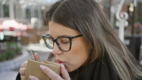 Eine Frau genießt eine keramische Tasse Kaffee in einem Outdoor-Café und betont urbane Freizeit und Stil. - Filmmaterial, Video