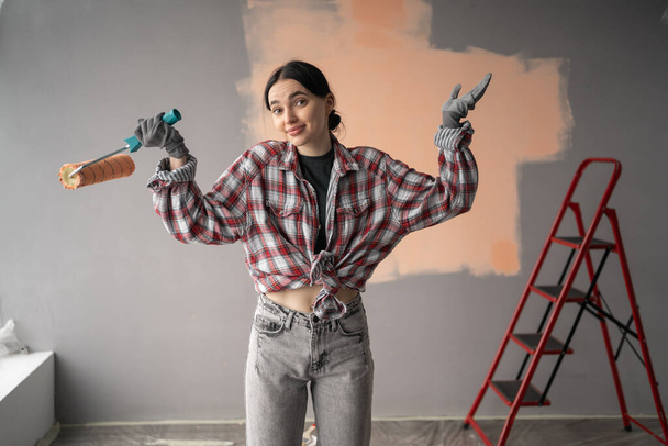 Sorprendido sorprendido pintor femenino con rodillo. Redecoración, renovación, concepto de reparación de apartamentos. - Foto, imagen