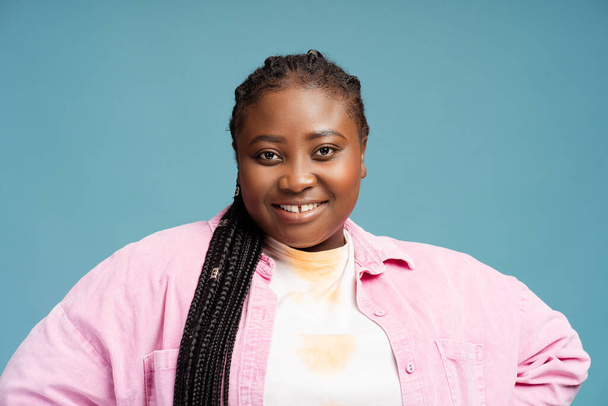 Beautiful modern African American woman with braids wearing stylish casual clothes looking at camera isolated on blue background. Smiling plus size model posing in studio. Advertisement concept - Foto, Imagen
