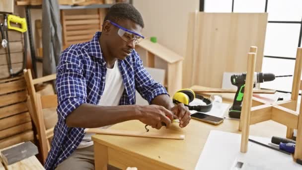 Сосредоточенный черный мужчина измеряет деревянную мебель в помещении мастерской. - Кадры, видео