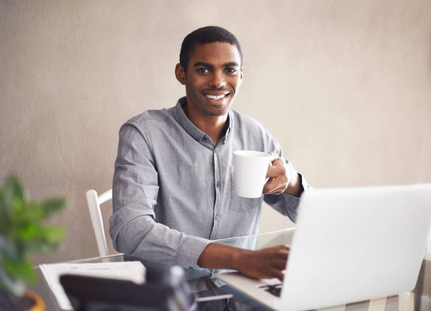 Πορτρέτο, πίνοντας καφέ και μαύρο laptop άνθρωπος για τις επιχειρήσεις στο γραφείο στο σπίτι, απομακρυσμένη εργασία ή πληκτρολογώντας email. Πρόσωπο, υπολογιστής ή χαμόγελο του ελεύθερου επαγγελματία με τσάι στο γραφείο, υπάλληλος ή copywriting για δημιουργικότητα. - Φωτογραφία, εικόνα