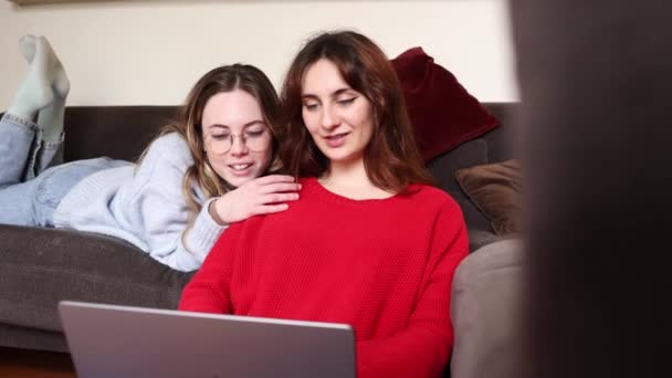 Female gay couple lie on the sofa in an intimate scene, conducting research on a laptop in their living room. Two lesbian women recline on the sofa, engaged in researching on a laptop in their living room. - Footage, Video