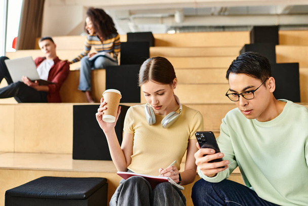 Bir erkek ve bir kadın, her ikisi de öğrenci, basamaklarda otururlar, cep telefonuna birlikte bakarlar. - Fotoğraf, Görsel