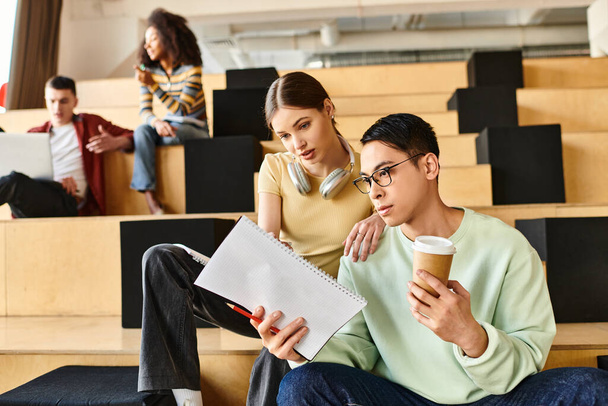 A man and woman, students, sit on a bench, studying a piece of paper with intense focus. Multicultural, indoor setting - Photo, Image