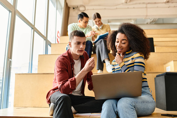 Мультикультурная группа молодых студентов, сидящих на ступеньках здания, сосредоточенная на экране ноутбука - Фото, изображение