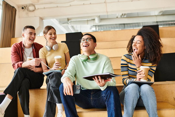 Estudantes multiculturais casualmente se sentam em um banco de madeira dentro de casa, desfrutando uns dos outros companhia - Foto, Imagem