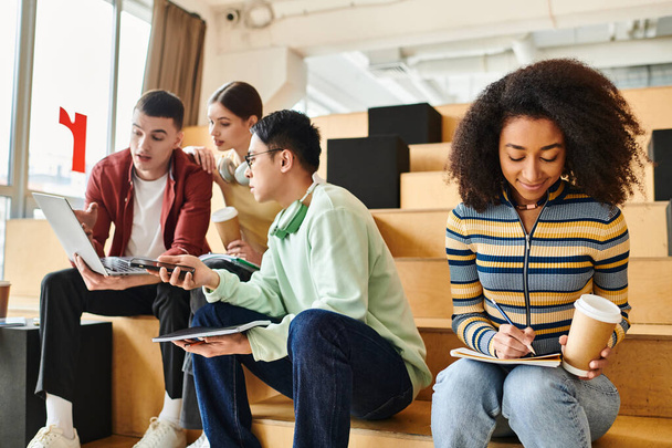 Groupe multiculturel d'étudiants s'engagent dans le travail de groupe sur les ordinateurs portables tout en étant assis sur les marches - Photo, image