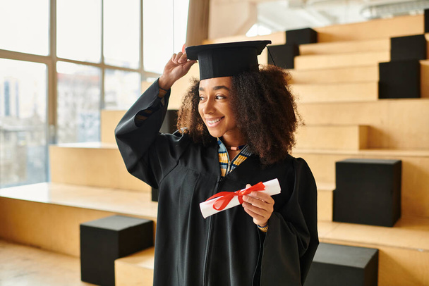 Молода афроамериканка з гордістю стоїть у випускній шапці і одязі, символізуючи академічний успіх і досягнення. - Фото, зображення