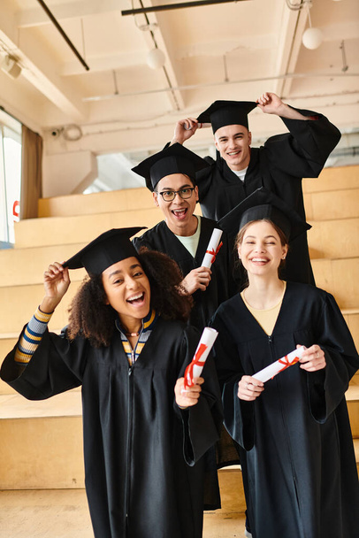 Diverso gruppo di studenti in abiti di laurea e berretti sorridenti per una foto di gruppo all'interno. - Foto, immagini