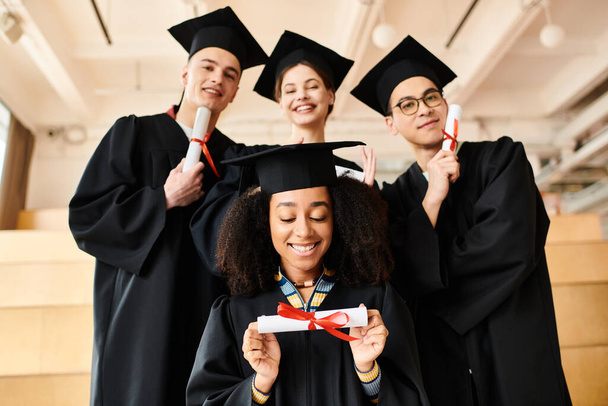 Разнообразная группа счастливых студентов в выпускных платьях и кепках позирует для праздничного фото в помещении. - Фото, изображение