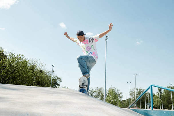 A young skater boy riding a skateboard up a ramp in a lively outdoor skate park on a sunny summer day. - Photo, Image