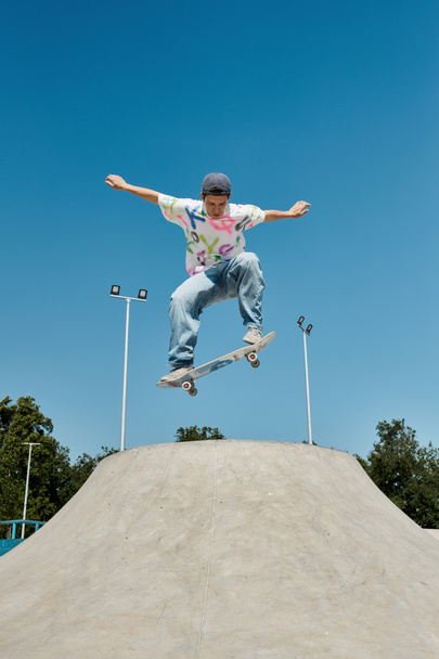A young skater boy defies gravity, soaring through the air on his skateboard at a sunlit skate park. - Photo, Image