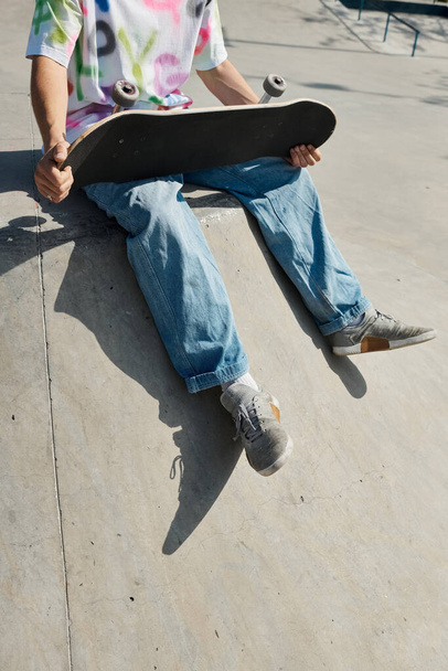 Een man zit op de grond, houdt een skateboard vast, diep in gedachten. - Foto, afbeelding