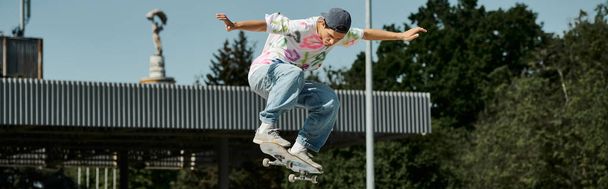 Młody łyżwiarz przeciwstawia się grawitacji podczas lotu w powietrzu podczas jazdy na deskorolce w skateparku w słoneczny letni dzień. - Zdjęcie, obraz