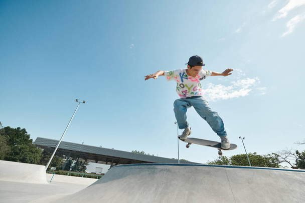 Ένα νεαρό αγόρι σκέιτερ με αυτοπεποίθηση βόλτες skateboard του μέχρι την πλευρά μιας ράμπας σε ένα υπαίθριο πάρκο skate σε μια ηλιόλουστη μέρα του καλοκαιριού. - Φωτογραφία, εικόνα