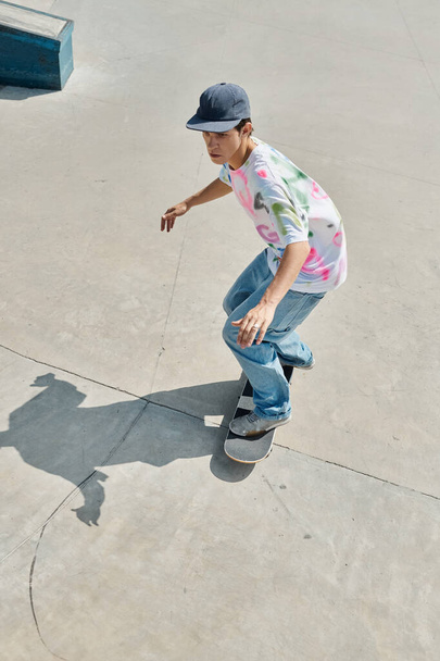 A young man effortlessly rides a skateboard down a cement ramp in a vibrant skate park on a sunny summer day. - Photo, Image