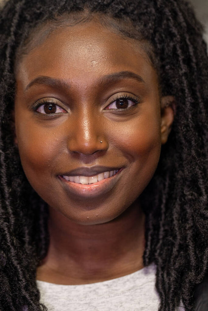 Das Foto zeigt eine junge schwarze Frau mit einem weichen und selbstbewussten Lächeln. Ihre natürliche Twist-Out-Frisur umrahmt ihr leuchtendes Gesicht perfekt und hebt ihre Augen hervor, die vor Lebendigkeit funkeln. Die - Foto, Bild