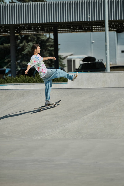 Ένα νεαρό αγόρι σκέιτερ με αυτοπεποίθηση βόλτες με ένα skateboard κάτω από την πλευρά μιας ράμπας σε ένα ζωντανό υπαίθριο πάρκο skate σε μια ηλιόλουστη μέρα του καλοκαιριού. - Φωτογραφία, εικόνα
